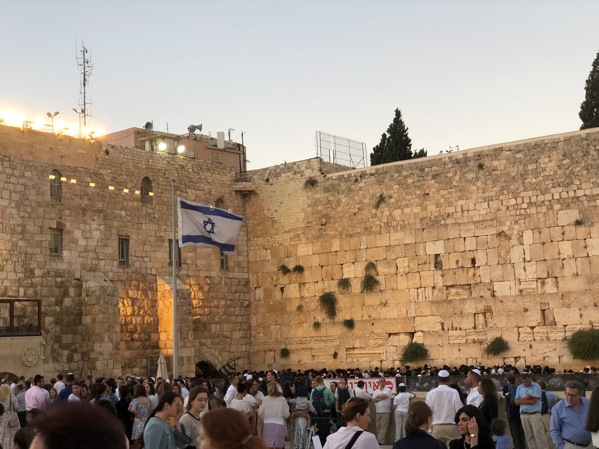 The Western Wall (Kotel) in Jerusalem's Old City at golden hour, packed with visitors praying and gathering at the base of the ancient stone wall